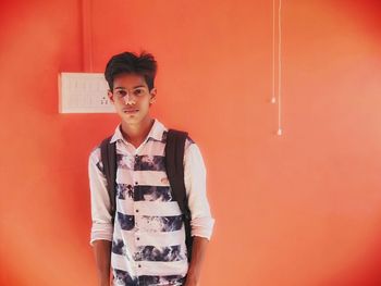 Portrait of young man standing against red wall