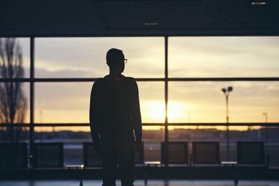 Silhouette man looking at sunset seen through window