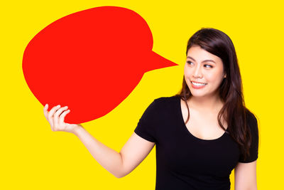 Portrait of smiling young woman against yellow background