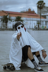 Portrait of young ghost in a spooky season  standing outdoors om a longboard