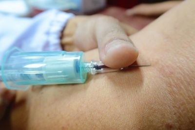 Cropped hand of doctor injecting patient at hospital