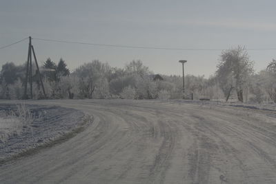 Road by trees against sky during winter