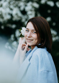 Portrait of happy smiling young woman with flower near her head in blooming park