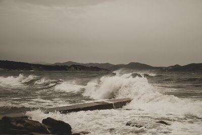 Waves splashing on shore against clear sky