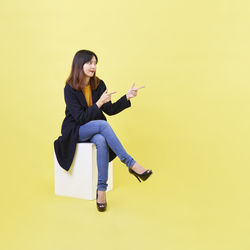 Side view of young woman sitting against yellow background