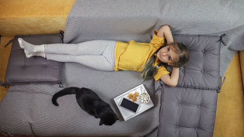 Directly above shot of girl relaxing on sofa with cat and food