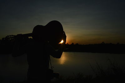 Silhouette man standing by lake against sky during sunset