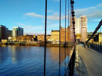 Bridge over river by buildings against sky in city