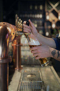 Midsection of bartender filling beer in bottle