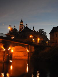 Illuminated building by river against sky at night