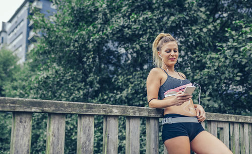 Young woman using mobile phone while sitting on bridge