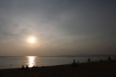 Silhouette people on beach against sky during sunset