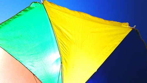 Low angle view of yellow parasol against blue sky