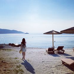 Rear view of woman sitting on beach against sky