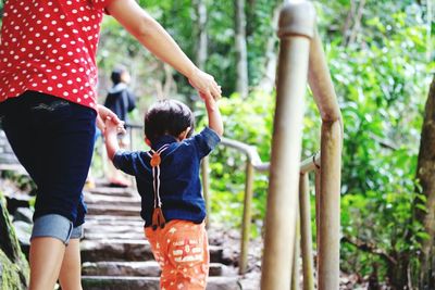 Rear view of mother climbing steps while holding hands with boy