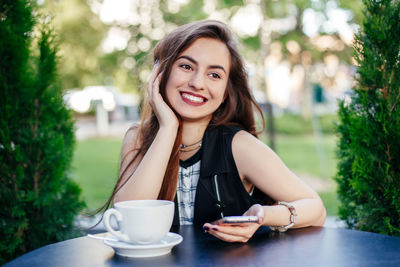 Smiling young woman using smart phone at outdoor cafe