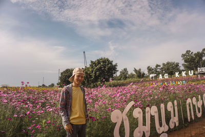Woman standing by pink flowering plants against sky