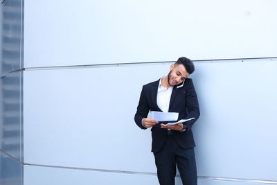 Young businessman reading document while talking on phone