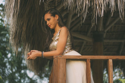 Low angle view of beautiful woman looking away while standing by railing under thatched roof
