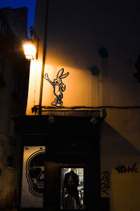 Silhouette of illuminated lamp by building against sky