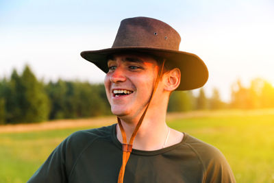 Young man smiling farmer in cowboy hat at agricultural field on sunset. candid portrait millennial