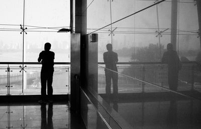 Rear view of silhouette man standing by railing on glass window