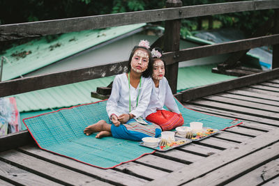 Portrait of cute girls with face paint sitting on boardwalk