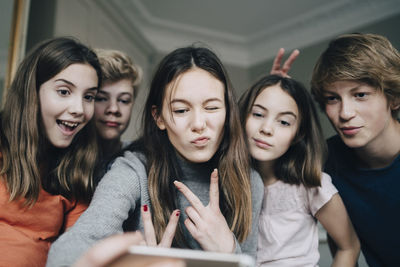 Cheerful friends taking selfie through mobile phone at home