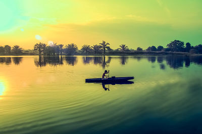 Side view of man rowing rowboat in lake against dramatic sky during sunset