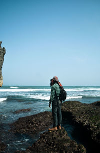 Full length of man standing on rock at beach against sky