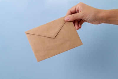 Close-up of hand holding paper against blue background