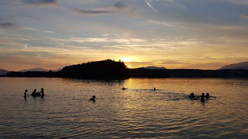 Silhouette people swimming in lake against sky during sunset