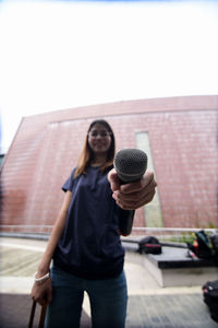 Portrait of female journalist with microphone standing against building