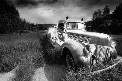 Abandoned car on grassy field against sky