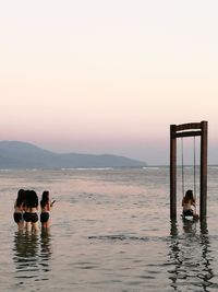 Women looking at friend swinging in sea against sky