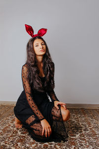 Portrait of young woman sitting against wall