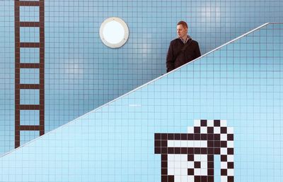 Man looking away while standing against tiled wall