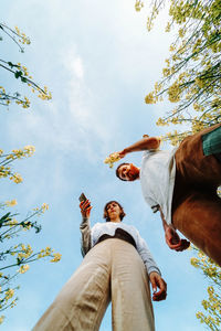 Low angle view of friends standing against sky