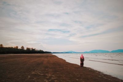 Rear view of woman standing on beach against sky