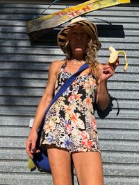 Low angle view of woman eating banana while standing against wall