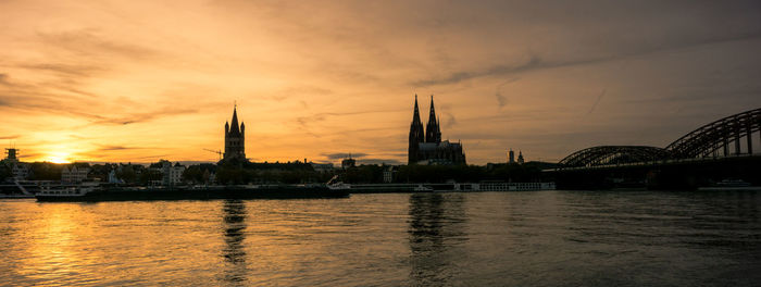 View of city buildings by river during sunset