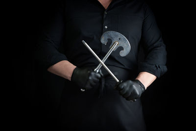 Midsection of man holding tools against black background