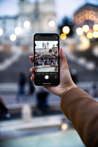 Cropped image of hand holding smart phone in city