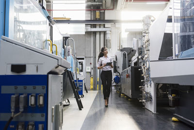 Woman with tablet at machine in factory shop floor lookig around