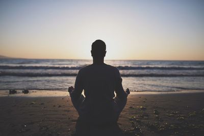 Young man in meditation near the sea. concept of pray. adult practice yoga on the beach at sunset.