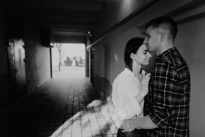 Side view of man kissing on woman forehead while standing indoors