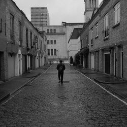 Rear view of man walking on road along buildings