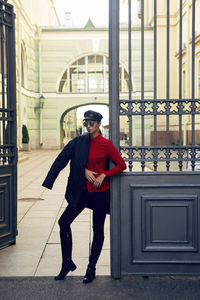 Woman stands at the iron gate in a black jacket on the street in sunglasses in autumn