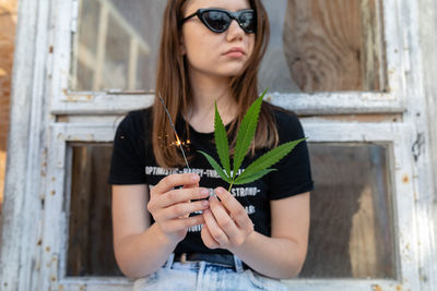 Young woman holding illuminated sparkler while sitting on wood