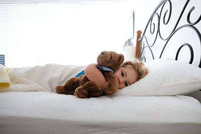Little girl laying in bed snuggling teddy bear looking at camera
